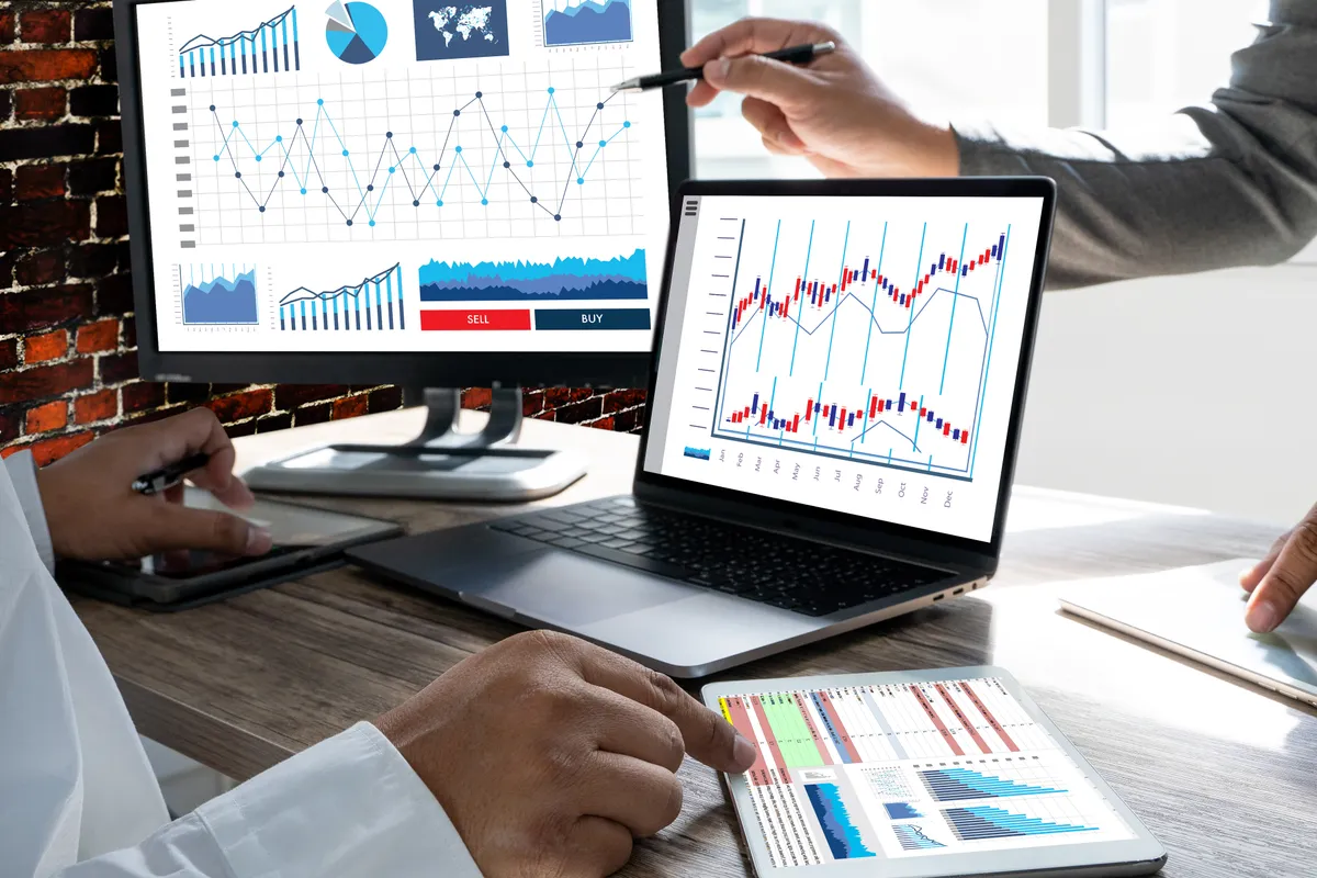 Profissionais analisando gráficos de previsão em um notebook e em relatórios impressos.